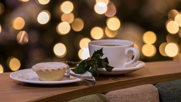 Mince pie and a cup of tea with a sprig of holly and background of fairy lights